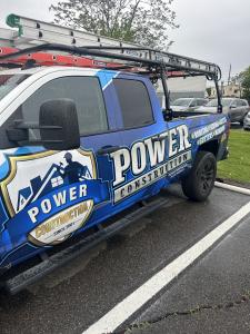 Blue Power Construction Inc. pickup truck with ladder rack, displaying roofing, siding, decks, gutters, and windows services.