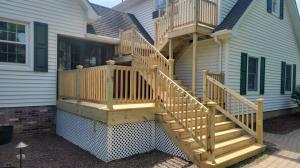 Newly built wood deck with staircase and railings attached to a white vinyl sided home.