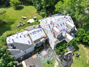 Aerial view of Power Construction roofing crew installing GAF synthetic underlayment on a two story home surrounded by trees.