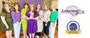 Group of seven smiling women standing indoors, three holding awards; LearningRx and IBCCES BCCC logos are displayed to the right.