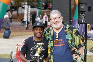 Two Atlanta Kosher BBQ Festival participants smile together while holding a BBQ competition trophy at the outdoor community festival.