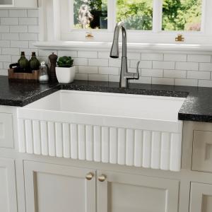 The same fireclay farmhouse sink installed with its plain smooth apron front facing out, set into cream cabinets under a dark countertop.