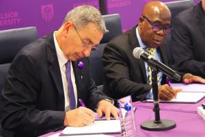 Two men sit at a table and sign a partnership agreement.