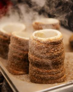 Warm cinnamon-sugar chimney cakes stand upright on a baking tray as steam rises around them.