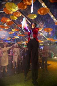 A colorful juggler on stilts juggles under a tent as costumed guest watch at the 2025 All Ghouls Gala