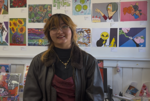 Alexandra “Lexi” Orr stands in front of a wall displaying colorful artwork at ECF’s South LA Art Center.