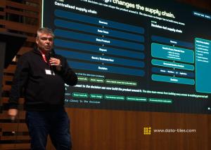 Cameron Price speaking on stage in Antwerp in front of a presentation showing centralized and decision-led data product supply chains.