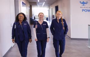 3 Galen students walking down a hallway in navy blue scrubs.