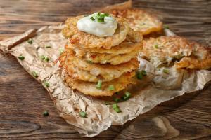 Stack of golden-brown potato pancakes topped with sour cream and chopped chives on a rustic wooden table.