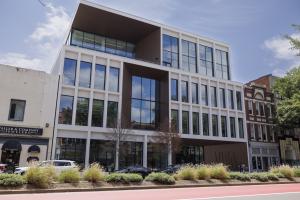 Exterior view of a VPM building with large glass windows situated on a street with landscaped flower beds and adjacent storefronts.