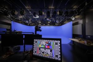 A television production studio featuring a large blue screen backdrop, overhead lighting rigs, and a foreground monitor displaying a VPM test pattern and "PCR-B"