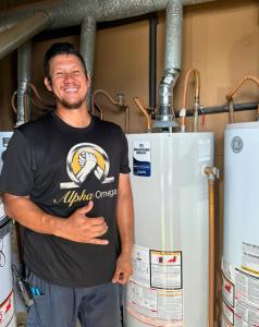 Alpha Omega Plumbing technician in a branded shirt standing beside newly installed water heaters.