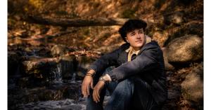 Cash Gaudio, a 19-year-old young man, sitting beside a river behind his family's home in Central Virginia.