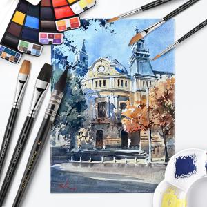 FUUMUUI watercolor brushes arranged around an architectural watercolor painting with watercolor palettes and painting tools.