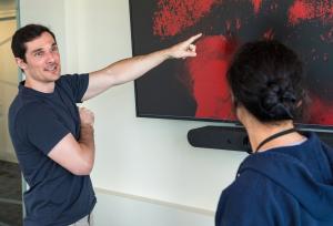 Male scientist pointing to a large computer monitor displaying a patter of red dots to a female scientists