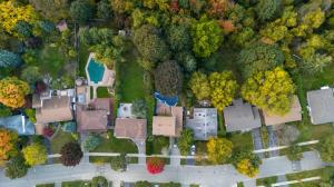 An aerial view of a suburban neighborhood in autumn, showing multiple rooftops, trees, and a backyard pool from above.