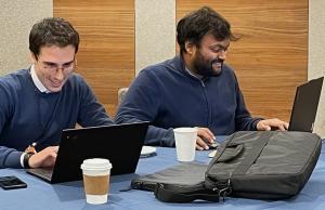 Two men sitting at a desk with the laptops open