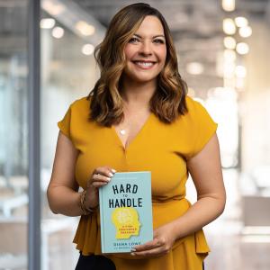 Diana Lowe, CEO of Blue Light Leadership, smiling and holding her book, Hard to Handle: A High Performer Paradox, in a modern office.