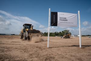 A wheel loader moves dirt across a cleared site beside a banner reading "Future Home, Occam Foundry, a quantum technology campus in Austin."