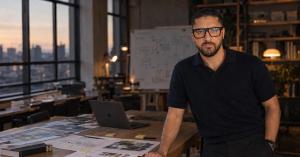 Portrait of Jacopo Spina, founding product designer and applied AI product engineer, leaning on a studio table covered in process maps and sticky notes, with a city skyline at dusk behind him