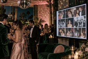 Wedding guests at an evening party with a My Glam Cam Glam Wall live photo slideshow on a large screen