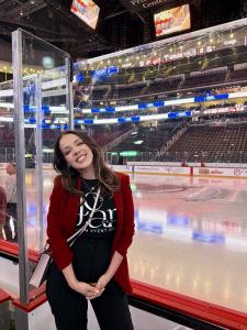 Jessenia Cosme, founder of JCsArtDesigns®, smiling in blazer with her logo shirt against the Devils Hockey Arena