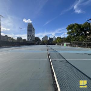 Empty McCarren Park tennis courts in daylight with new LED sports light poles along both sides and the Williamsburg skyline behind.