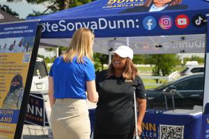 Maryland Comptroller Brooke Lierman, left, shakes hands with Sonya Dunn, who smiles in front of her campaign tent at an outdoor event in Anne Arundel County