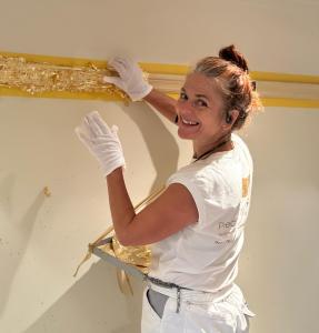 Krissie Mayne hand-applying traditional gold leaf gilding to a bespoke interior wall in Australia