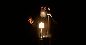 Jon Schnitzer a bearded man picks up a 1980s landline phone only lit by a small lamp surrounded by darkness. It looks spooky because it's from "Something Spooky".