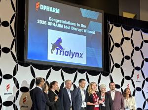 Angie Schwab, Founder and CEO of Trialynx, stands on stage after being named the 2026 DPHARM Idol Disrupt winner, surrounded by members of the judging panel.