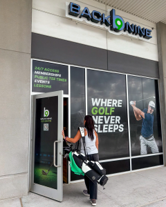 Indoor golf Elkhorn at Back Nine Golf, featuring a golfer carrying her clubs into the 24/7 facility offering public tee times, memberships and lessons.