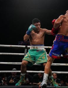 Isaac “Pitbull” Cruz throws a punch at Néstor Bravo in the boxing ring while wearing green shorts featuring the Adriana’s Insurance logo.