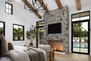 Sitting area with a wood-beamed vaulted ceiling, chandelier, stone fireplace and black-framed glass doors overlooking the pool.