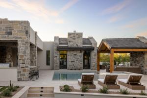 Backyard pool with lounge chairs, an outdoor kitchen and a covered seating pavilion surrounded by stone-clad architecture.
