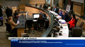 King County Council members and staff seated at the dais during a Committee of the Whole meeting, with laptops, monitors, and microphones at each position and a King County Council seal visible on the wall.