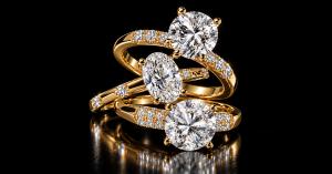 Three yellow gold moissanite engagement rings featuring round and oval center stones on a black reflective background