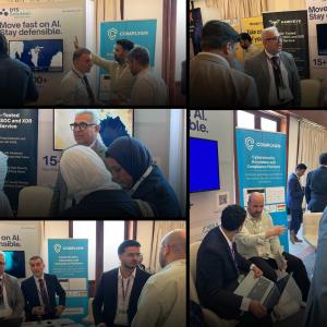 DTS Solution team members standing at their CYSEC Kuwait 2026 stand, speaking with visitors in front of a HawkEye managed CSOC and XDR banner, a "Move fast on AI. Stay defensible." DTS Solution backdrop and a Complyan banner.