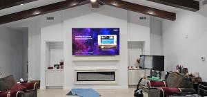 TV installation El Paso service above a modern linear fireplace and mantel, in a high-ceiling living room with wooden beams.