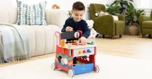 Young child playing with the Jasey's Toy Chest On-the-Go Wooden Workbench, a wooden push-walker and activity set