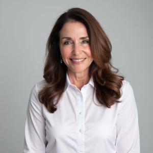 Picture of a middle aged female with dark hair and a light top looks straight at the camera