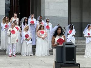 A group of women wearing wedding dresses with back tape in the shape of an X, protesting for California to introduce a law against child marriage