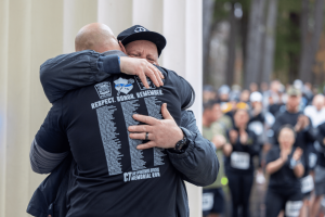 Two people embrace at the 2023 Connecticut Law Enforcement Officers Memorial Run as one wears a “Respect. Honor. Remember.” shirt displaying the names of fallen officers.