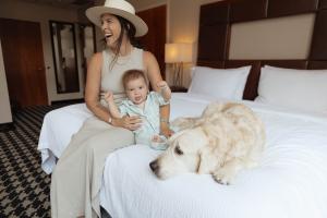Family (mom, baby, and dog) sitting on a King-size bed in a Courtyard Denver Downtown pet-friendly hotel room.