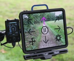 A person driving a power wheelchair using Ability Drive, eye-gaze enabled arrows displayed on an iPad that shows the surrounding enviornment.