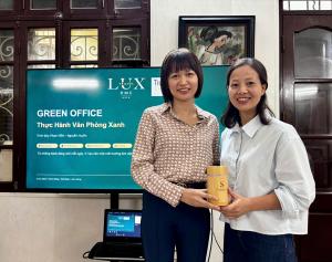Deux collaboratrices de Lux Travel DMC tiennent un objet cylindrique en bambou devant un écran affichant « Green Office » et le logo de l’entreprise.