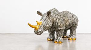 Midas Hart’s rhinoceros sculpture covered in U.S. dollar bills, with gold horns and toenails, standing on a pale floor against a white background.