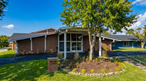 Main entrance to building with driveway, landscaping, shady trees