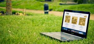 A laptop sitting in a grassy park displays the PowerCorpsPHL homepage, showing the navigation menu and three photo tiles for Partnership, Careers, and Support.