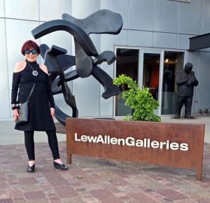A woman in contemporary clothing and glasses standing in front of a contemporary art gallery